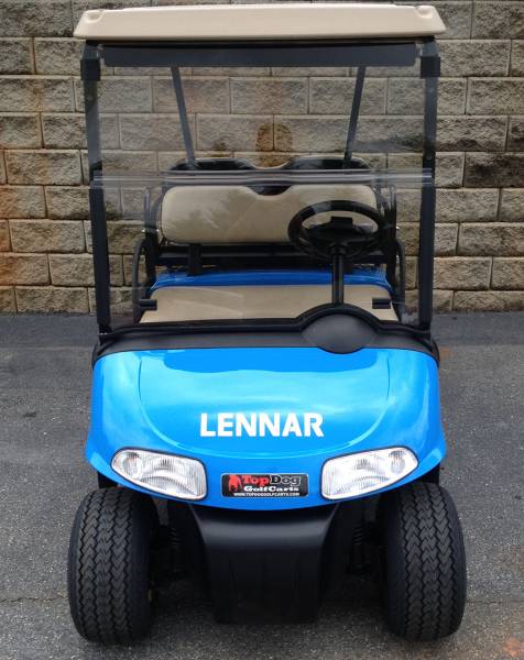 Blue golf cart with "LENNAR" written on the front, parked on asphalt in front of a stone wall.