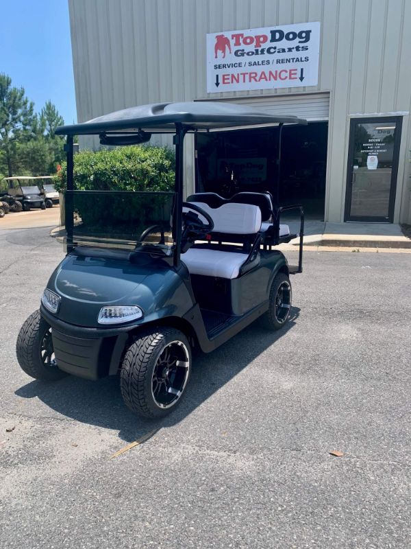 A black golf cart with white seats is parked outside a building with a "Top Dog Golf Carts" sign above the entrance.