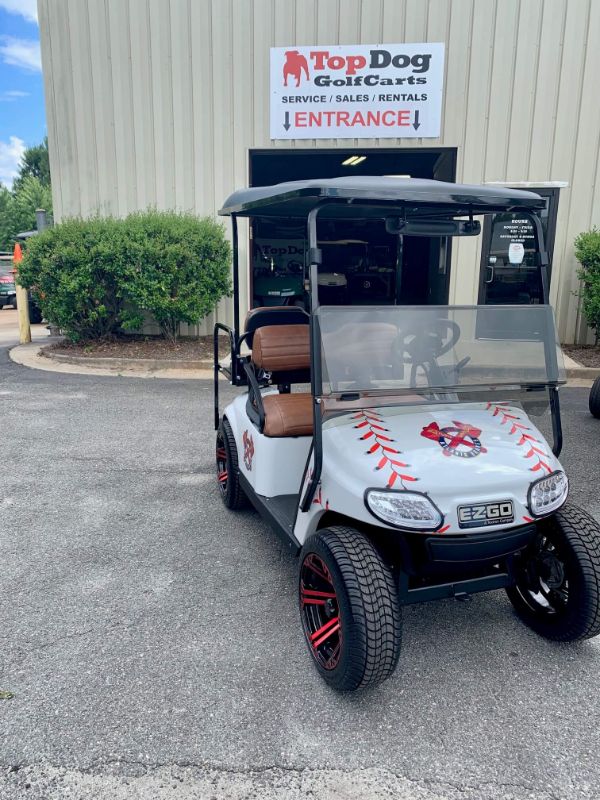 A custom EZGO golf cart with red and black accents is parked outside Top Dog Golf Carts, a store offering service, sales, and rentals.