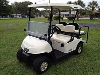 A white golf cart with beige seats is parked on a grassy area near a residential neighborhood.