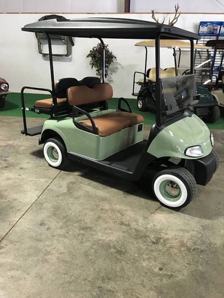 A green golf cart with brown seats and whitewall tires is parked indoors on a concrete floor.