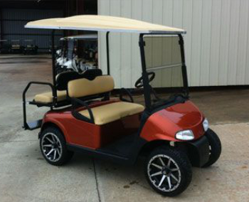A red and beige golf cart with black accents and a white roof is parked on a concrete surface near a metal building.